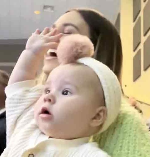 Mom glows with happiness as the infant raises his hands in praise.
